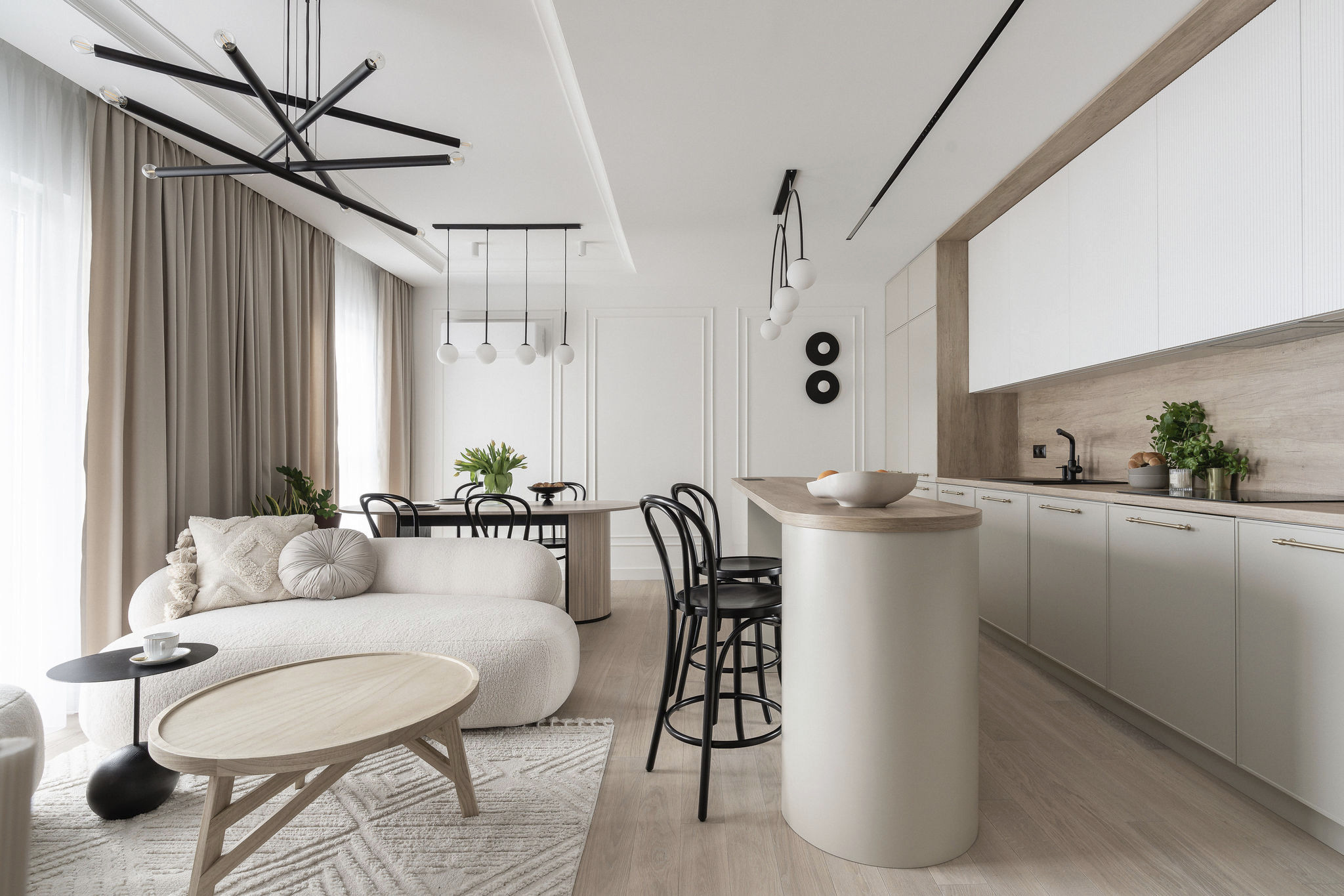 Jasne, przestronne wnętrze: sofa boucle, stolik, krzesła barowe, stół z tulipanami i nowoczesna kuchnia z drewnianymi akcentami. Minimalistyczny design i eleganckie oświetlenie.