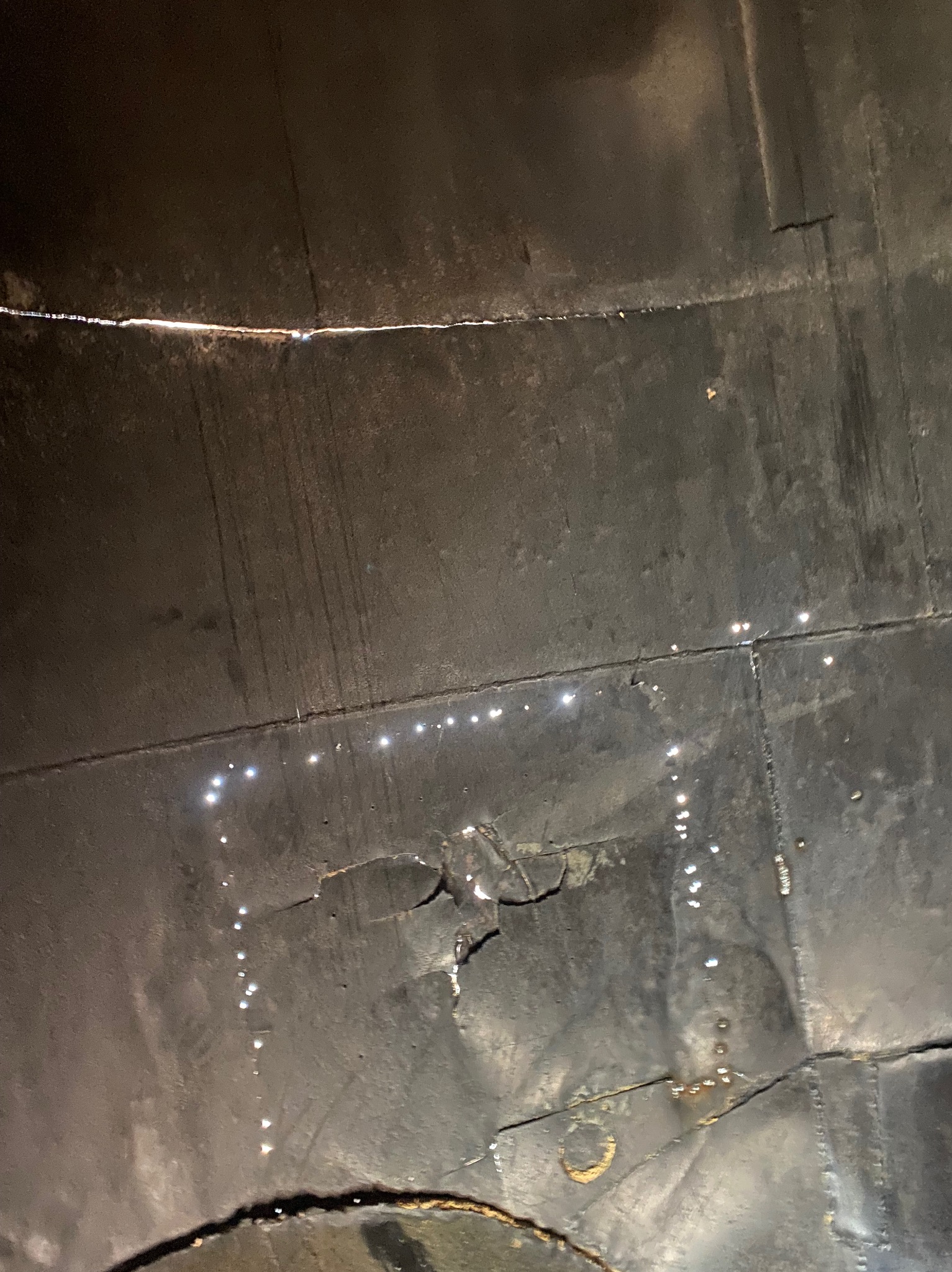 Wnętrze zbiornika metalowego z widocznymi spawami i śladami korozji, ukazujące strukturę i łączenia blach. Nietypowe ujęcie od wewnątrz.