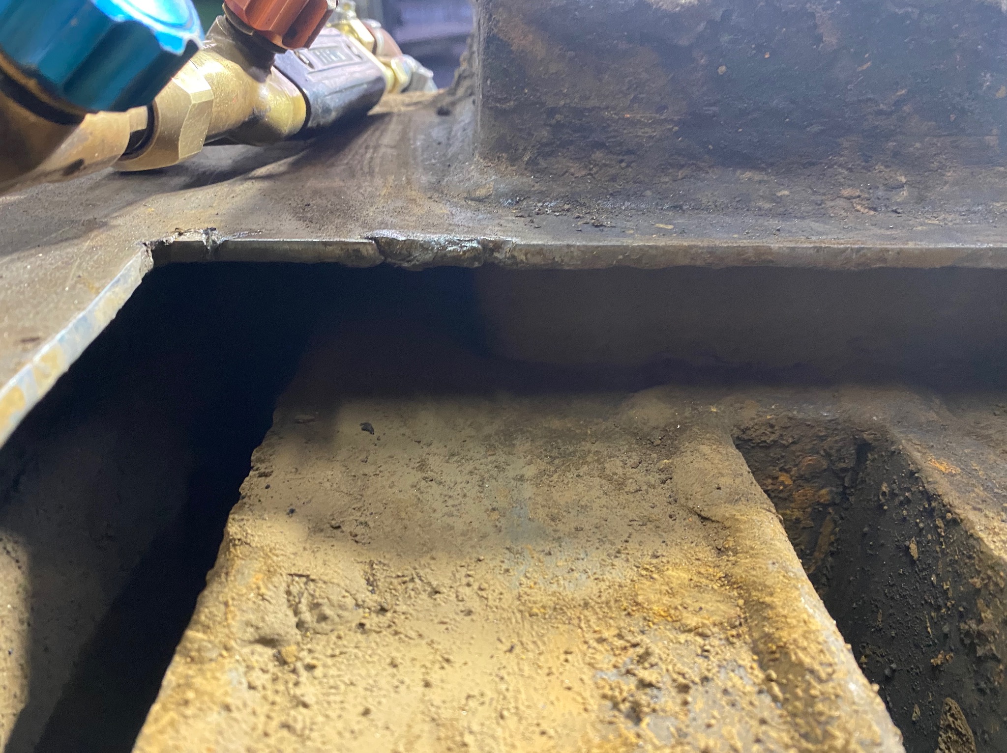 Fragment metalowej konstrukcji z widocznymi śladami spawania i obróbki, zbliżenie na spoinę. Widoczne narzędzia spawalnicze w tle. Surowy detal metalu.