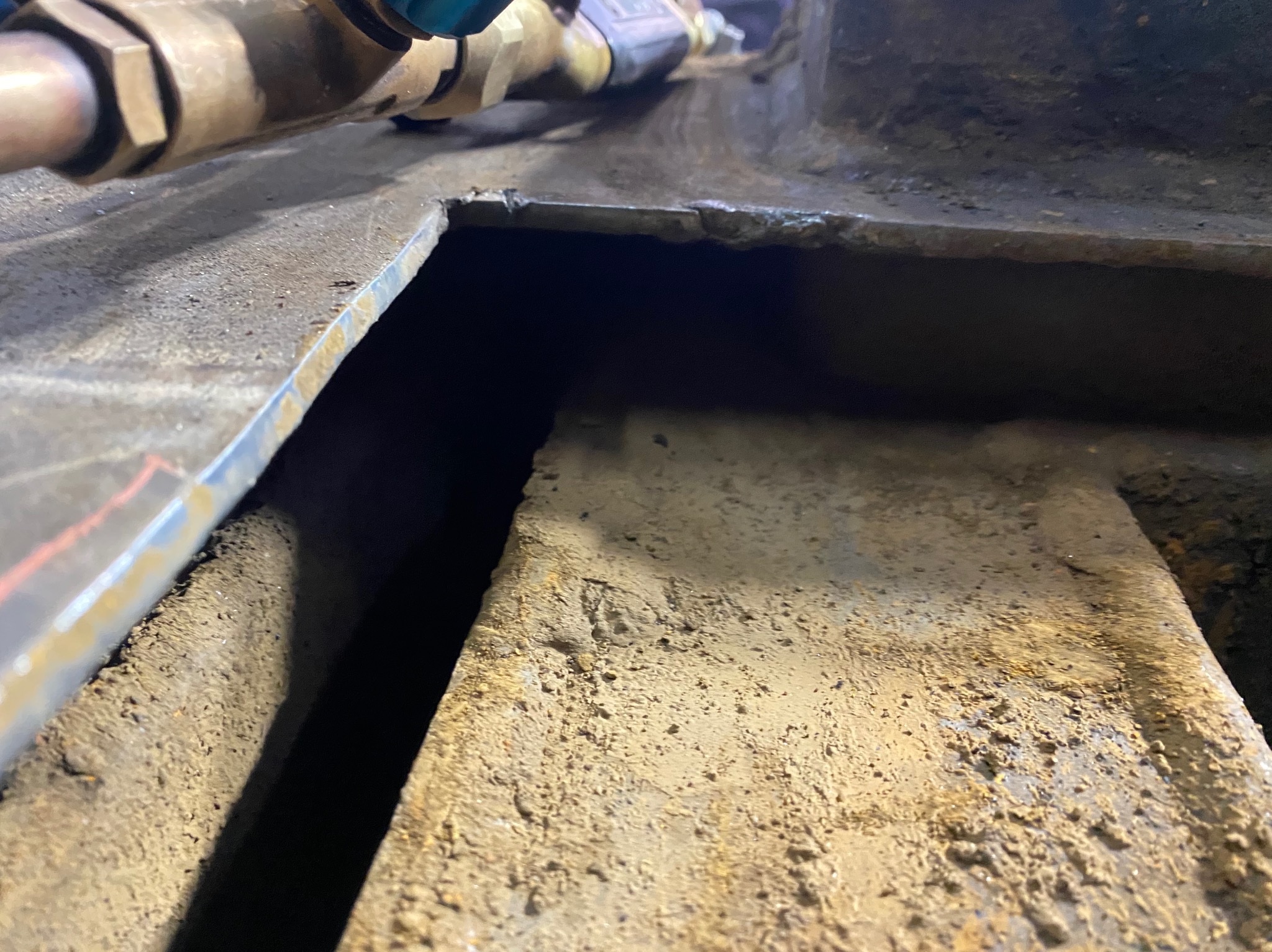 Metalowa konstrukcja z widocznymi śladami korozji i obróbki, z fragmentami instalacji hydraulicznej w tle. Ukazane detale i tekstura materiału.