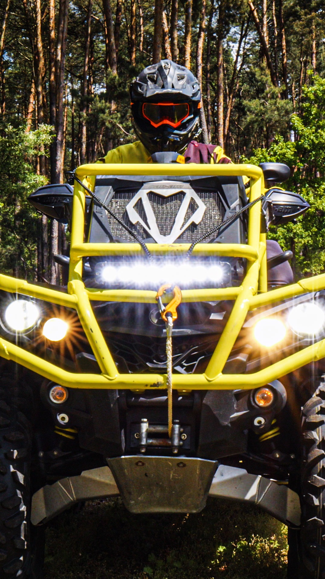 Żółty quad z kierowcą w kasku na leśnej trasie w okolicach Poznania. Widok z przodu, ostre światło reflektorów. Wyraźne opony i elementy zawieszenia.