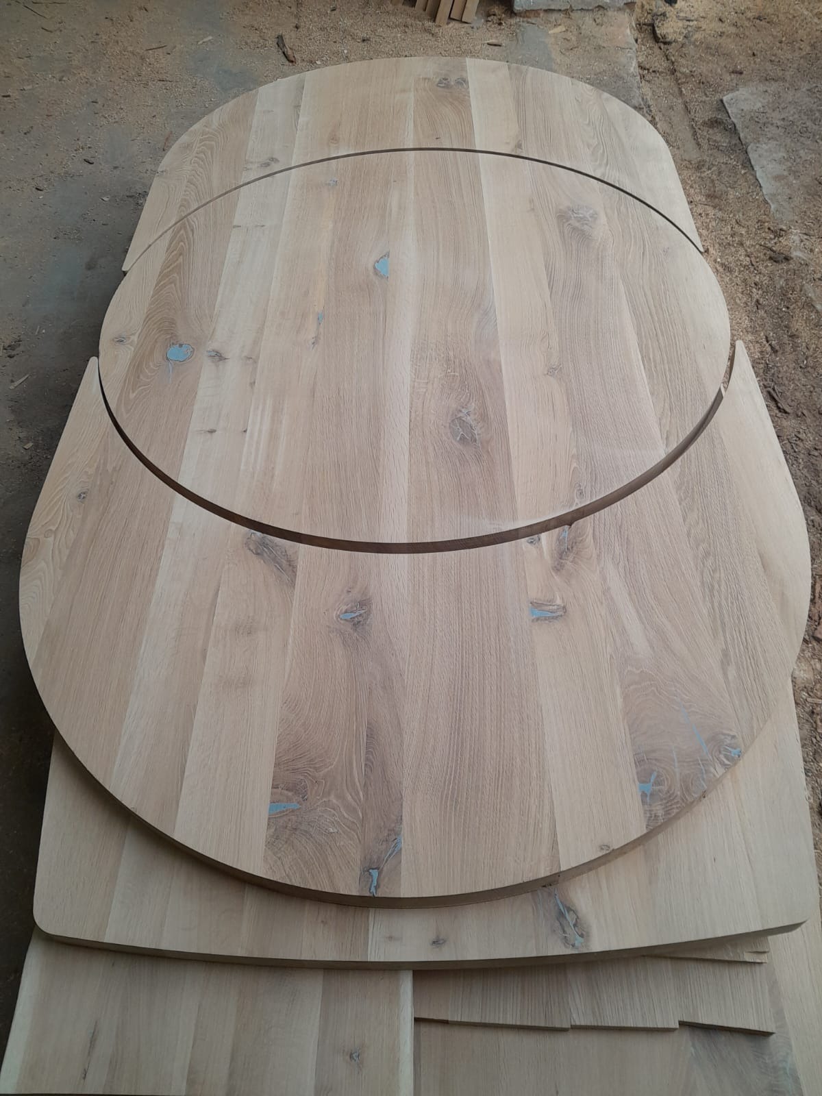 Blaty drewniane z jasnego drewna dębowego, okrągłe i półokrągłe, ułożone jeden na drugim. Widoczne słoje i naturalne niedoskonałości drewna. Surowe wykończenie.