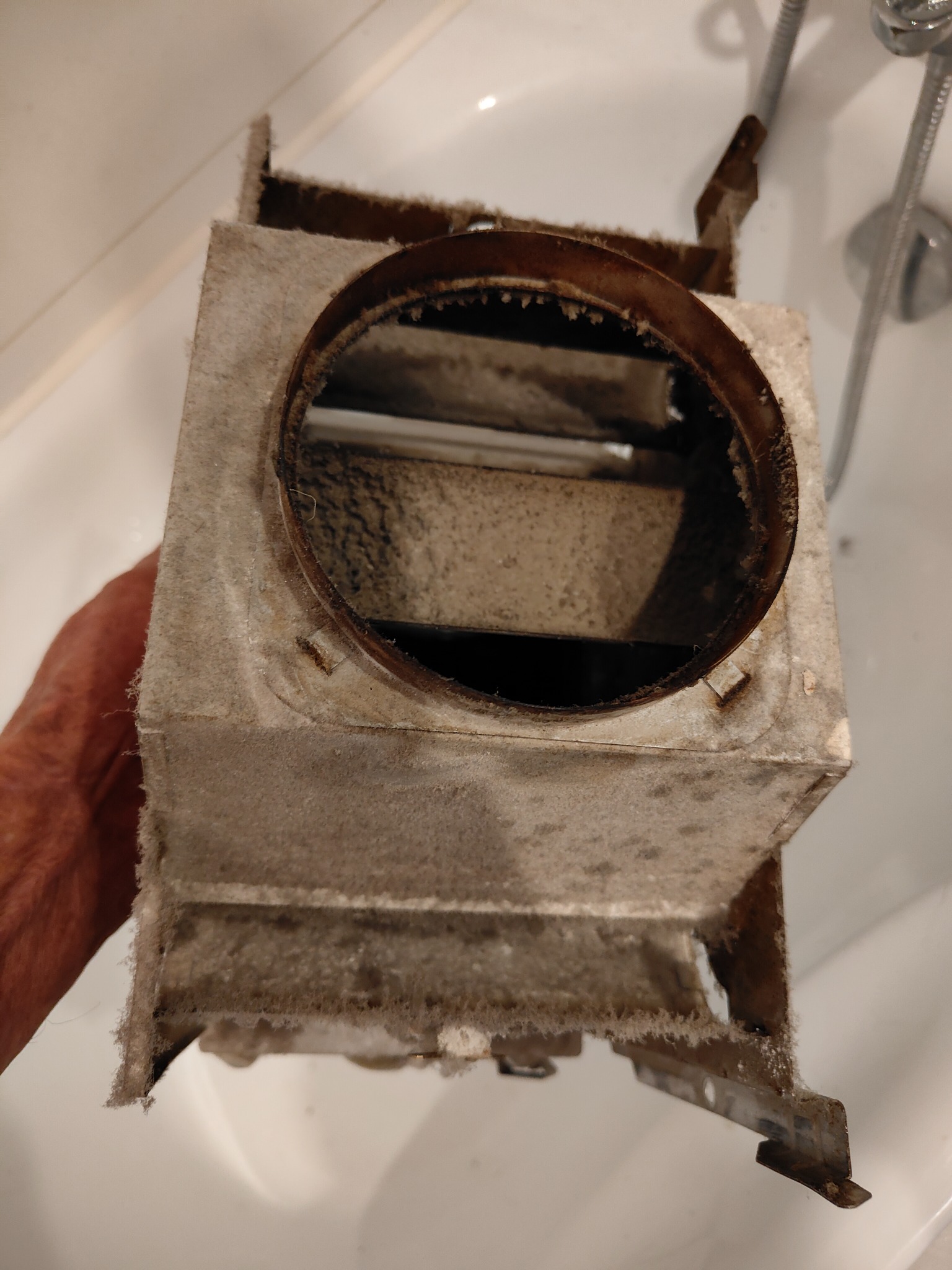 Zdemontowany, silnie zabrudzony element pieca gazowego z widoczną rdzą i osadami, trzymany nad białą umywalką w łazience. Widoczny fragment dłoni.