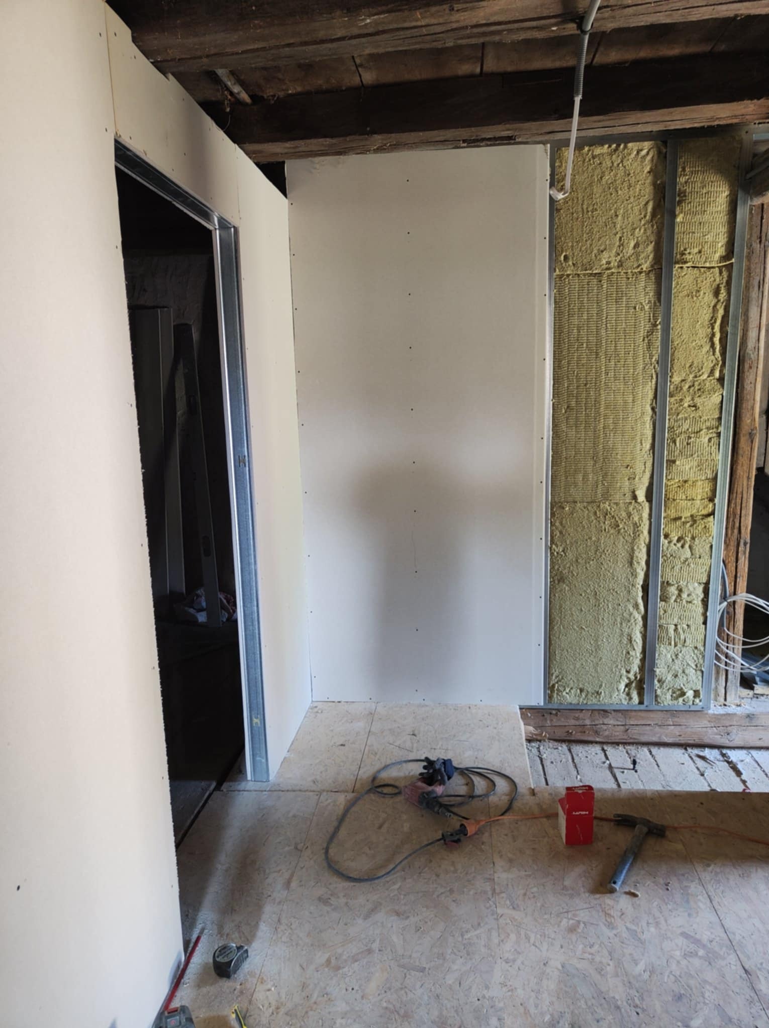 Wnętrze w trakcie montażu ścian z płyt karton-gips, widoczne profile metalowe, izolacja z wełny mineralnej i narzędzia na podłodze z desek.