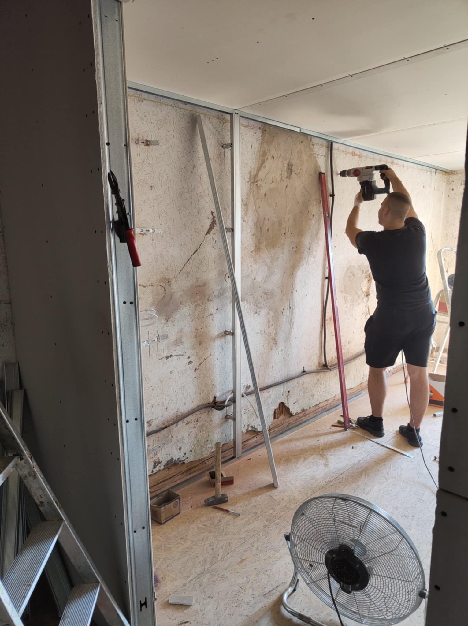 Prace przygotowawcze do montażu płyty karton-gips: pracownik wierci w metalowym profilu na ścianie. Widoczne narzędzia i materiały budowlane.