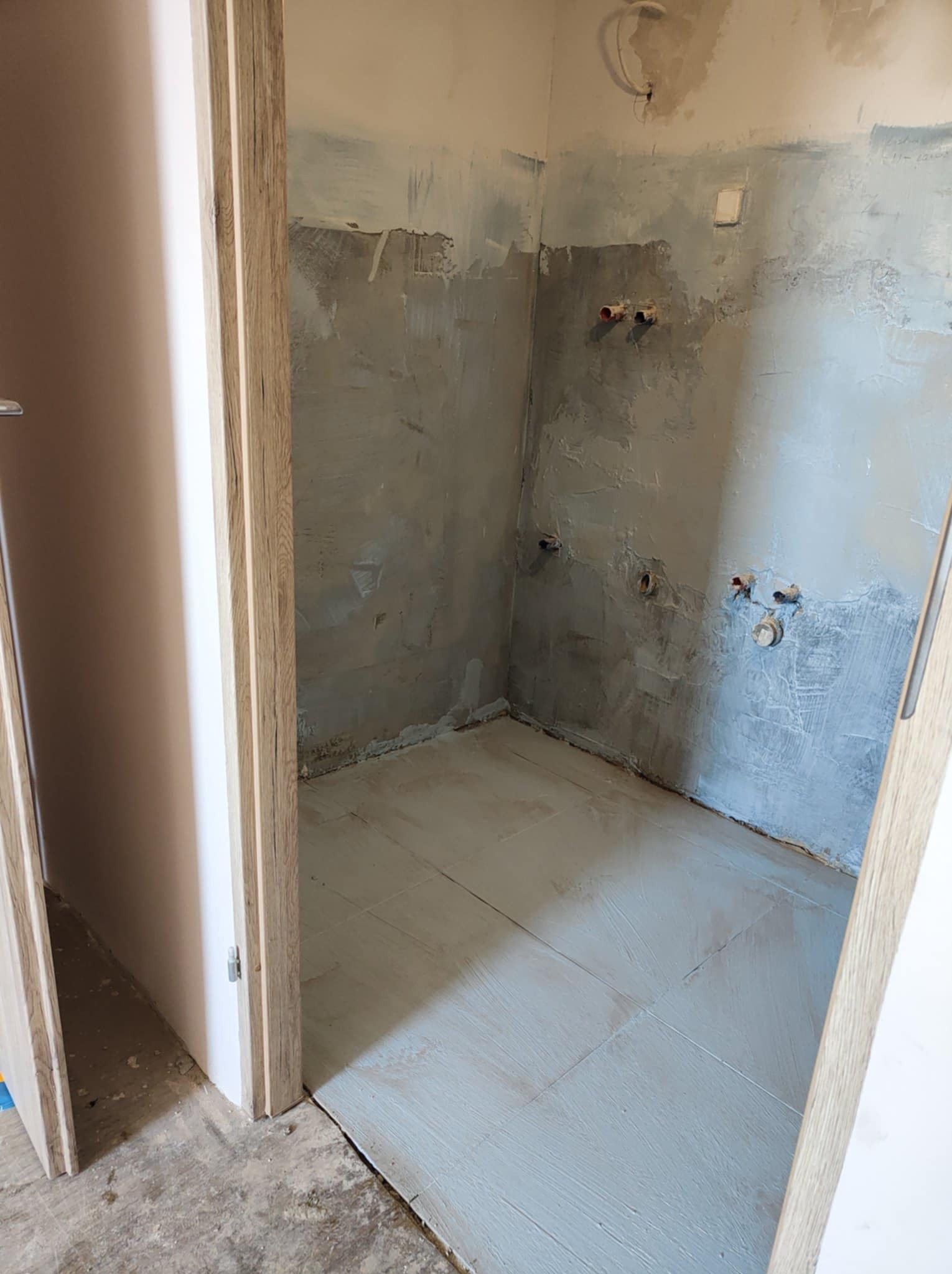 Łazienka w trakcie remontu w Opolu: położone płytki podłogowe, ściany po szpachlowaniu, widoczne instalacje wodne, przygotowane do dalszych prac wykończeniowych.