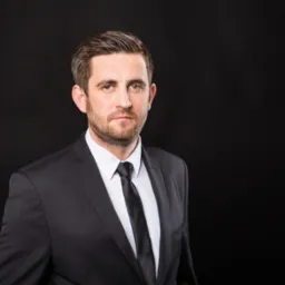 Portret biznesowy mężczyzny w czarnym garniturze i białej koszuli na ciemnym tle. Powaga i profesjonalizm w spojrzeniu.