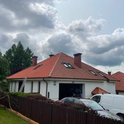 TECHO Wiktor Krupa - Dom jednorodzinny z czerwoną dachówką, drabina oparta o ścianę, widoczny samochód osobowy i dostawczy. Pochmurne niebo w tle.