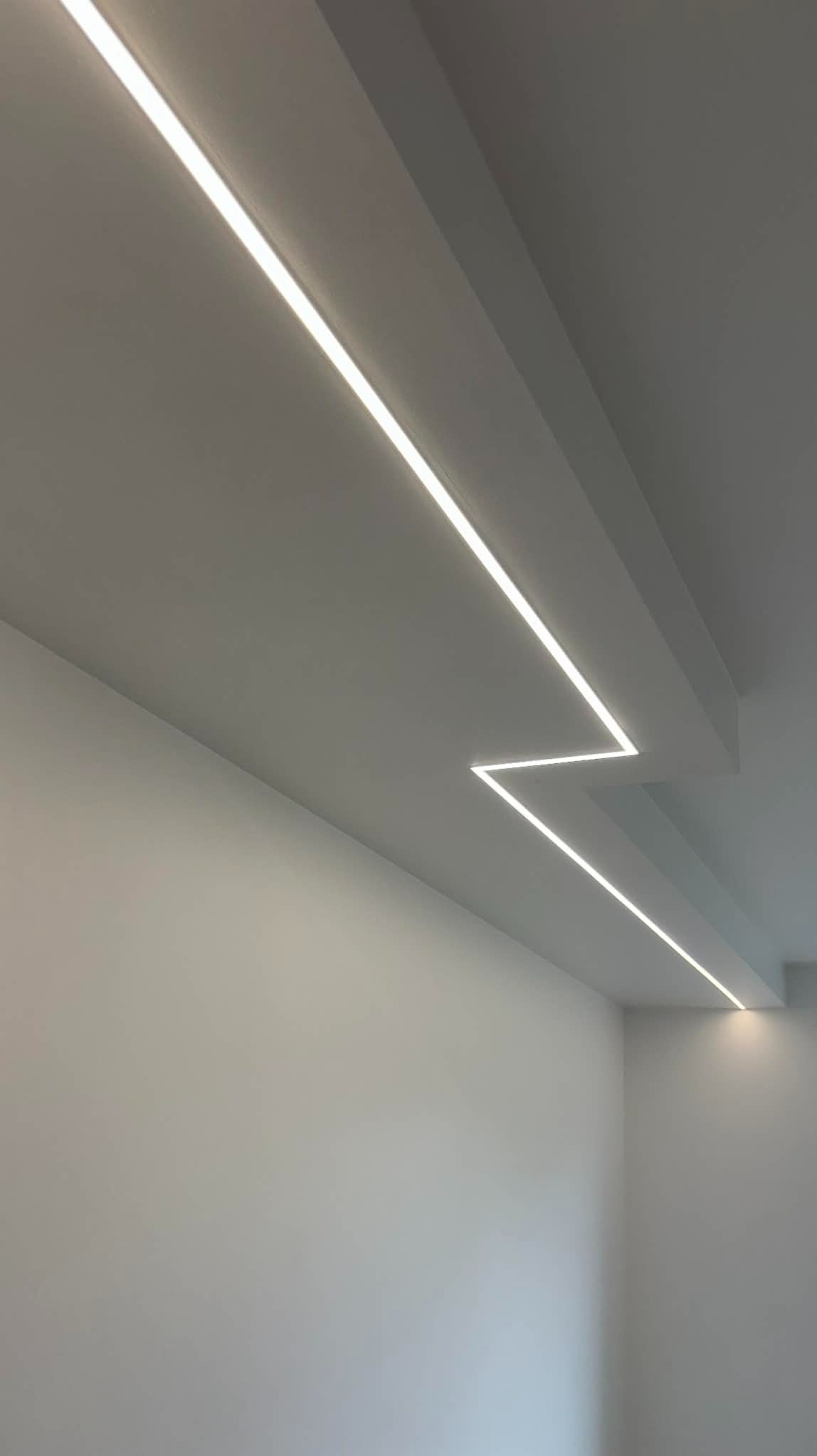 Minimalistyczne oświetlenie LED w suficie podwieszanym, tworzące geometryczny wzór w jasnym, nowoczesnym wnętrzu. Widoczne precyzyjne wykończenie i równomierne światło.