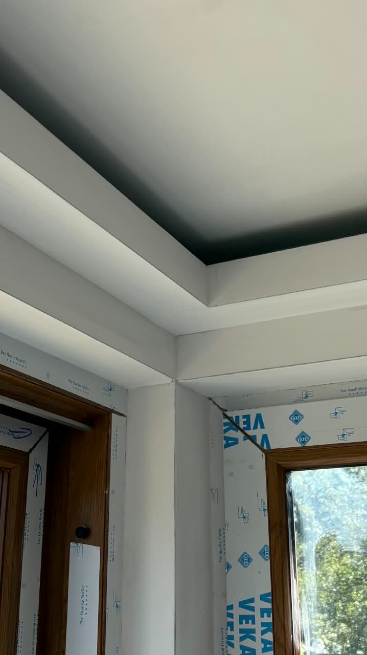 Wykończony sufit podwieszany z oświetleniem wnękowym, widok z narożnika pokoju, okno z profilem VEKA, drewniane drzwi. Jasne, nowoczesne wnętrze po remoncie.