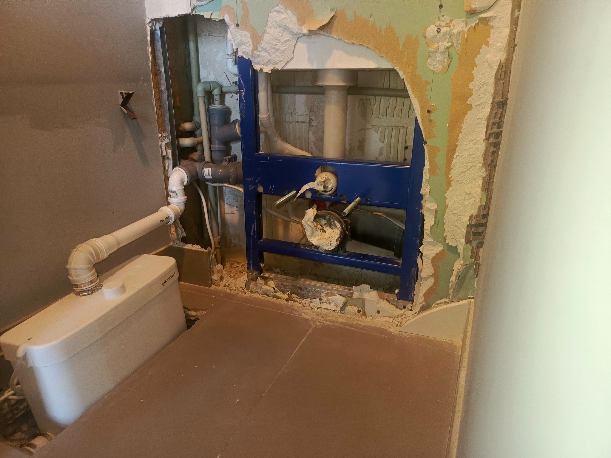 Montaż stelaża podtynkowego WC z widocznymi rurami i syfonem w trakcie remontu łazienki. Fragmenty starej farby na ścianie.