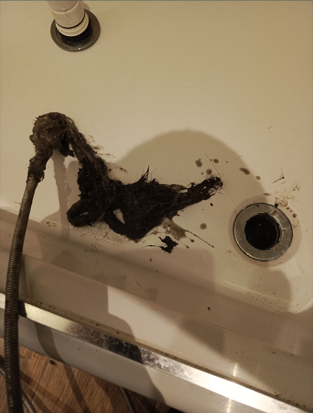 Udrożniona umywalka z wyciągniętymi zanieczyszczeniami i narzędziem do udrażniania. Widoczne resztki i zabrudzenia po wykonanej usłudze.