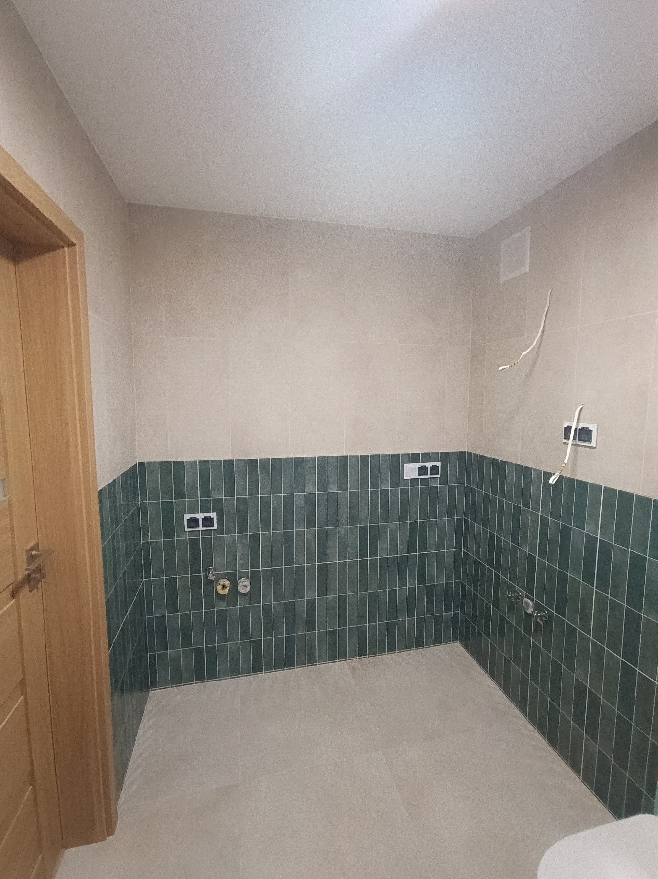 Wykończona łazienka w Warszawie z zielonymi płytkami do połowy ściany i beżowymi powyżej. Widoczne instalacje i biała ceramika. Nowoczesny design.