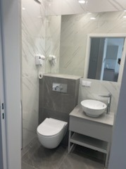 Nowoczesna, wykończona łazienka w Warszawie z marmurowymi płytkami, podwieszaną toaletą i umywalką nablatową. Minimalistyczny design, oświetlenie punktowe.