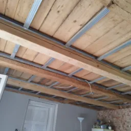 Drewniany strop z metalową konstrukcją podwieszaną, przygotowany do montażu płyt karton-gips. Widoczne elementy instalacji elektrycznej.