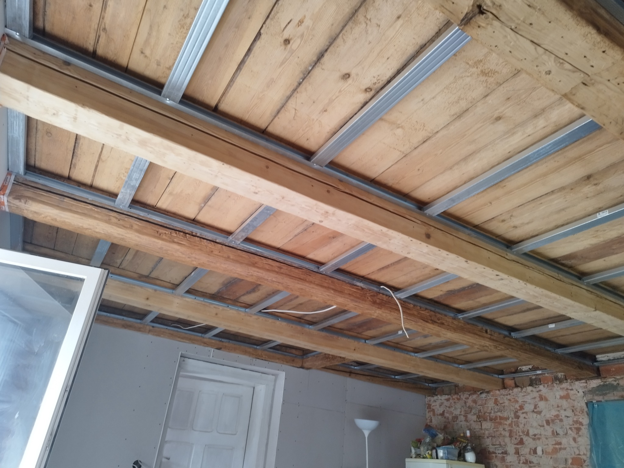 Drewniany strop z metalową konstrukcją podwieszaną, przygotowany do montażu płyt karton-gips. Widoczne elementy instalacji elektrycznej.