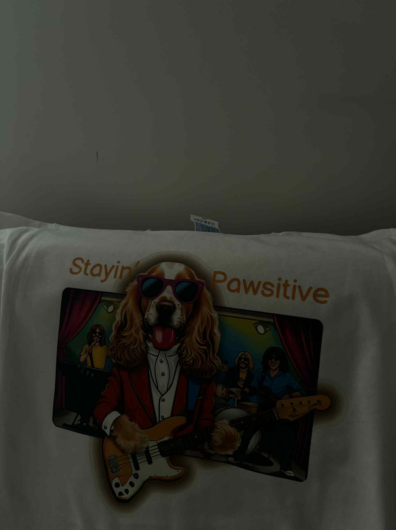 Biała koszulka z nadrukiem psa w garniturze i okularach, grającego na gitarze basowej, z napisem 'Stayin' Pawsitive'.