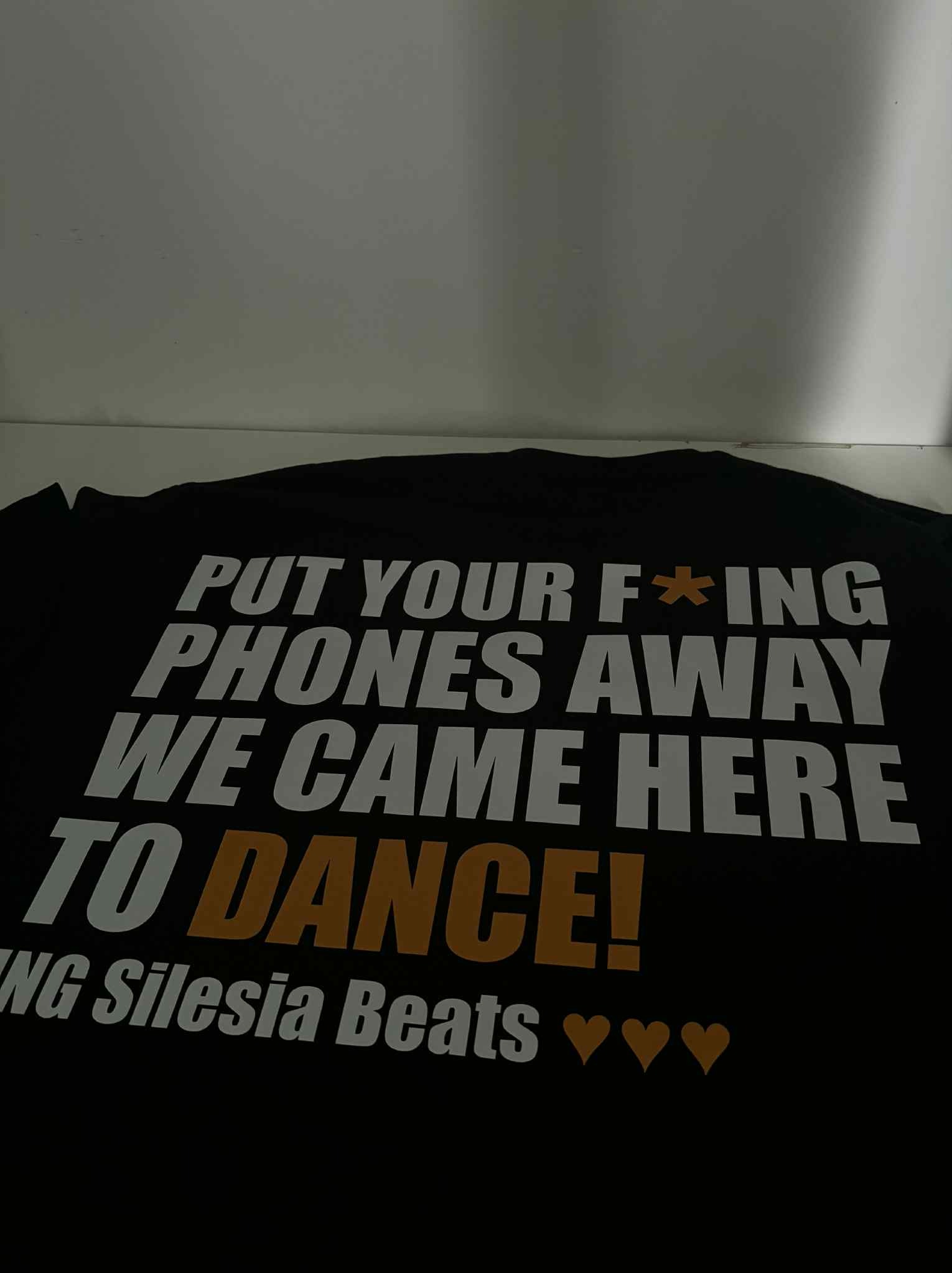 Czarna koszulka z białym i pomarańczowym nadrukiem: 'PUT YOUR F*ING PHONES AWAY WE CAME HERE TO DANCE!' oraz 'ING Silesia Beats' z trzema sercami.