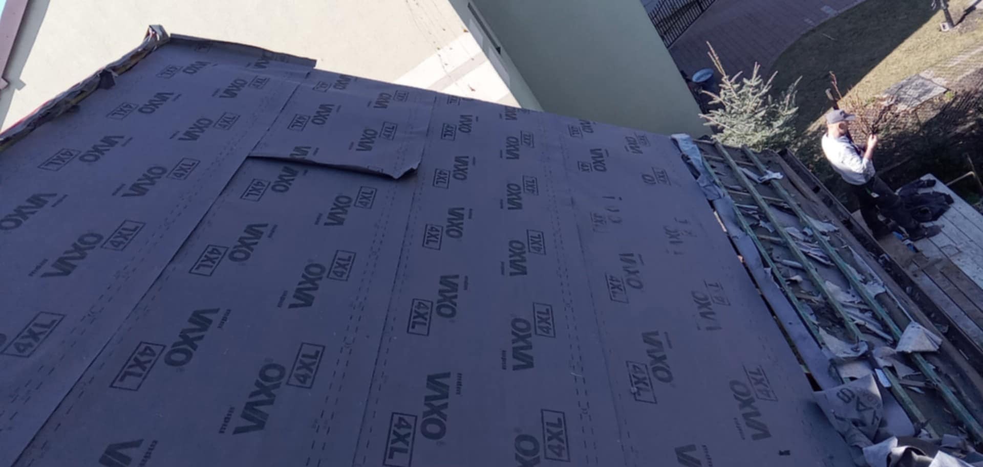 Dach w trakcie krycia papą z widoczną membraną dachową Vaxo 4XL, z fragmentem więźby i pracującym dekarzem w tle.