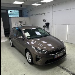 Filo Autokosmetyka - Brązowa Kia Ceed po myciu w jasnym pomieszczeniu myjni, z widocznymi certyfikatami na ścianie i kratką odpływową w posadzce. Oświetlenie sufitowe podkreśla czystość.