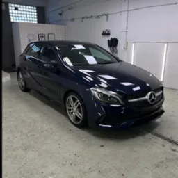 Błyszczący, granatowy Mercedes klasy A po detailingu w jasnym garażu. Widoczne oświetlenie LED, kratka ściekowa i certyfikaty na ścianie.