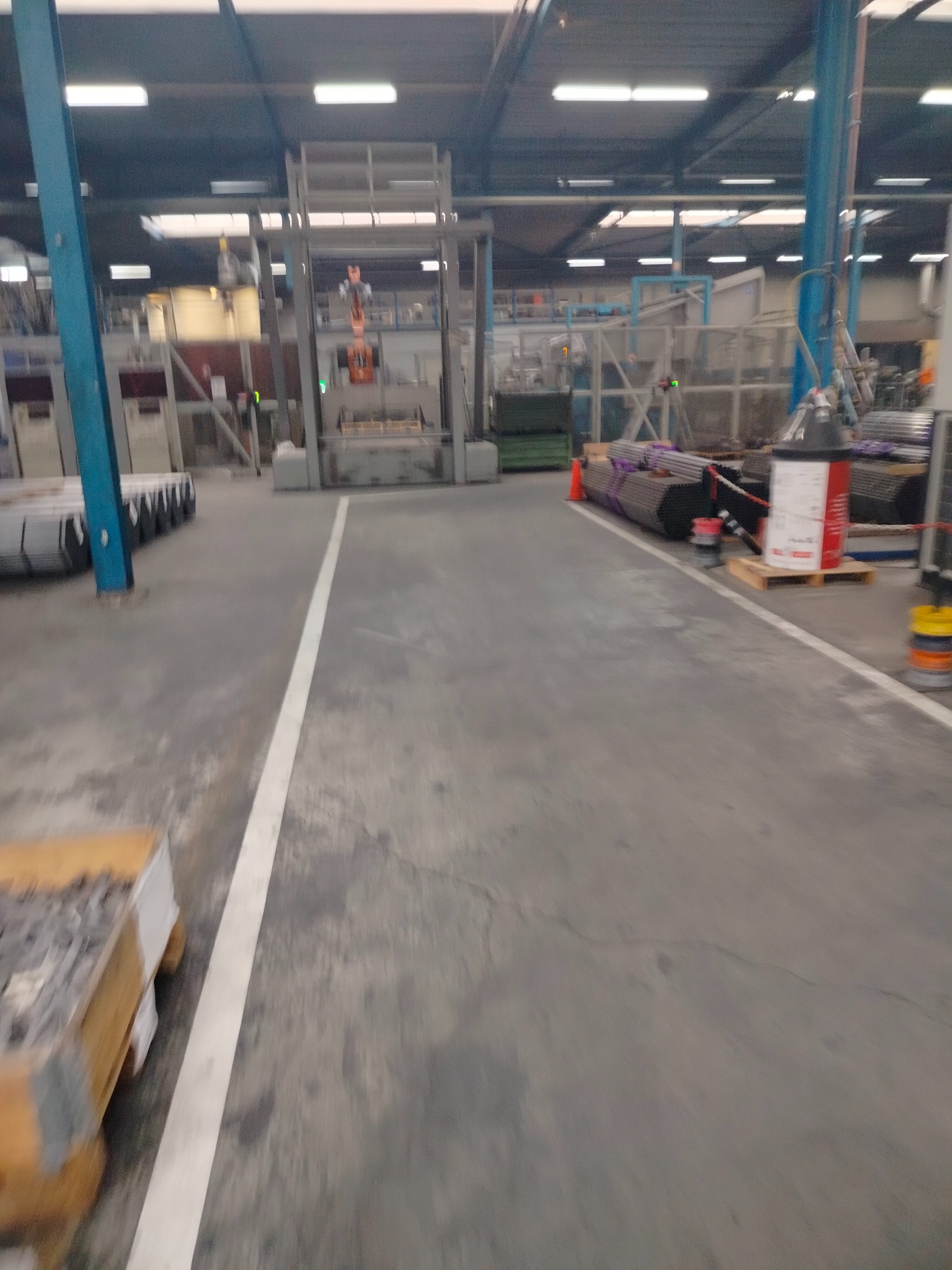 Wnętrze hali produkcyjnej z metalowymi elementami i konstrukcjami. Widoczne rury, profile i maszyny do obróbki metali. Oświetlenie przemysłowe.