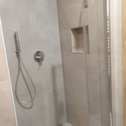 Jasna kabina prysznicowa z beżowymi płytkami i wnęką. Nowoczesny design, chromowana armatura. Widok z bliska na detale wykończenia.