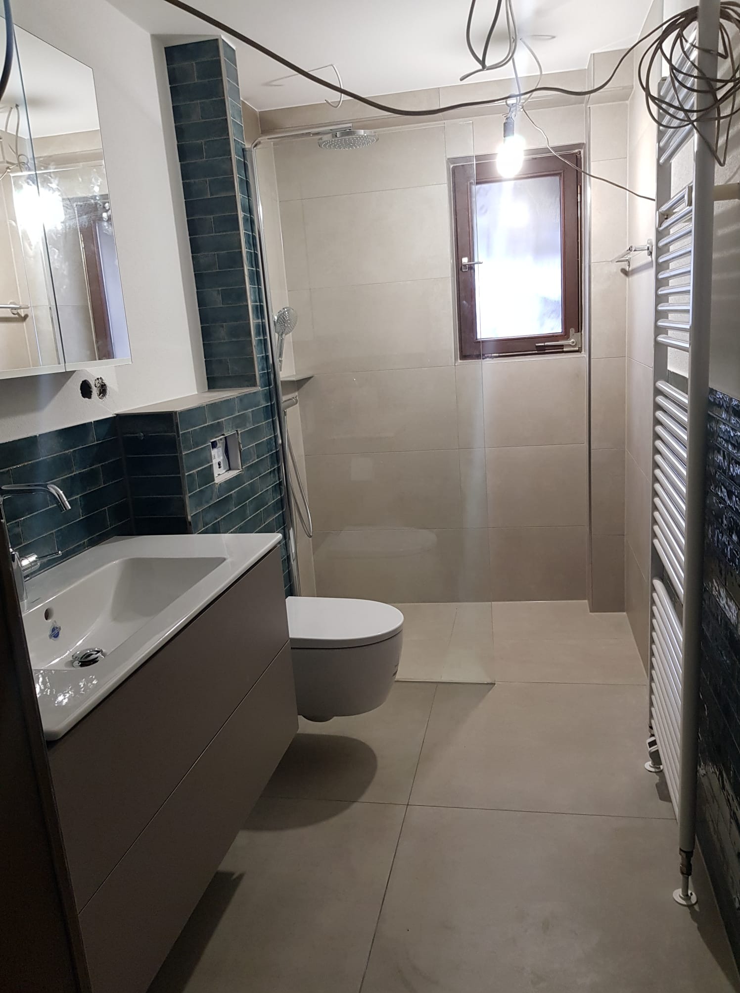 Nowoczesna łazienka z umywalką nablatową, toaletą i grzejnikiem drabinkowym. Ściany wyłożone beżowymi i ciemnymi, cegiełkowymi płytkami. Widoczne przewody elektryczne.