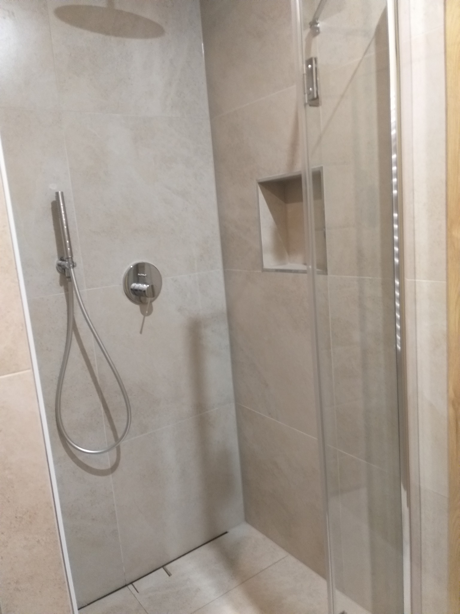 Jasna kabina prysznicowa z beżowymi płytkami i wnęką. Nowoczesny design, chromowana armatura. Widok z bliska na detale wykończenia.