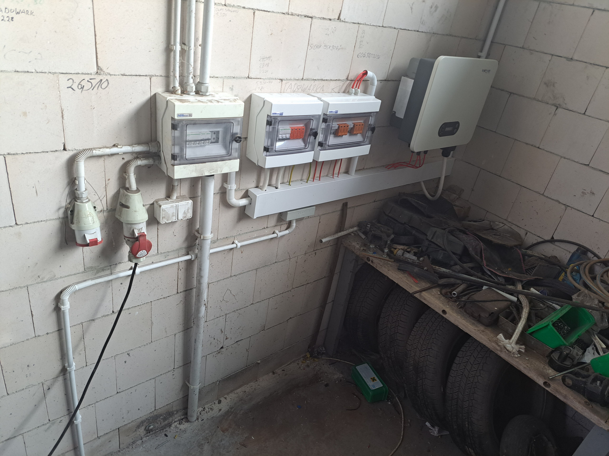 Zamontowana instalacja elektryczna z rozdzielnicami i falownikiem SOFAR na ścianie z białego bloczka, widoczne przewody i gniazda. Przykładowa realizacja.