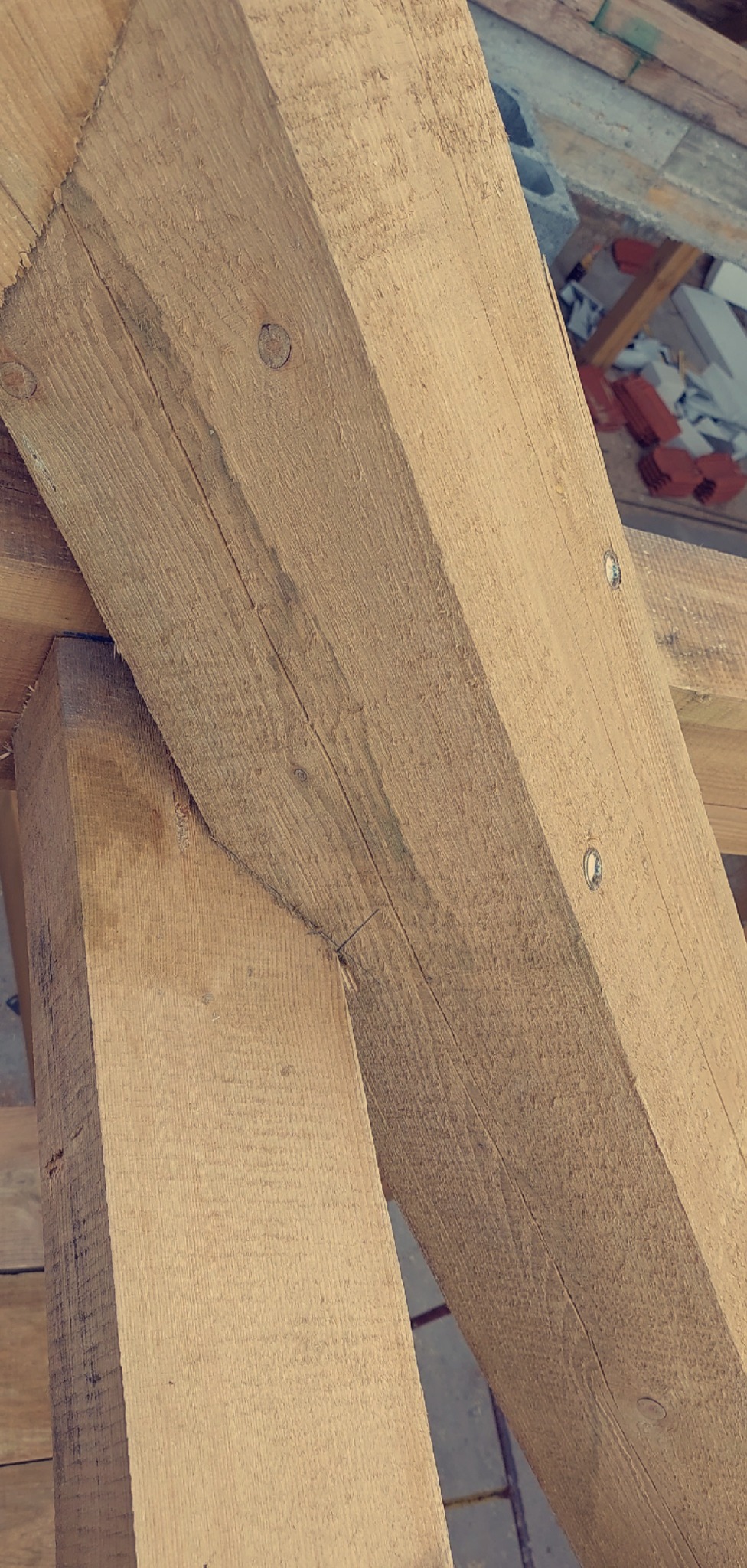 Drewniana więźba dachowa z widocznymi połączeniami i elementami mocującymi, ukazana z bliska w trakcie montażu. Konstrukcja z surowego drewna.