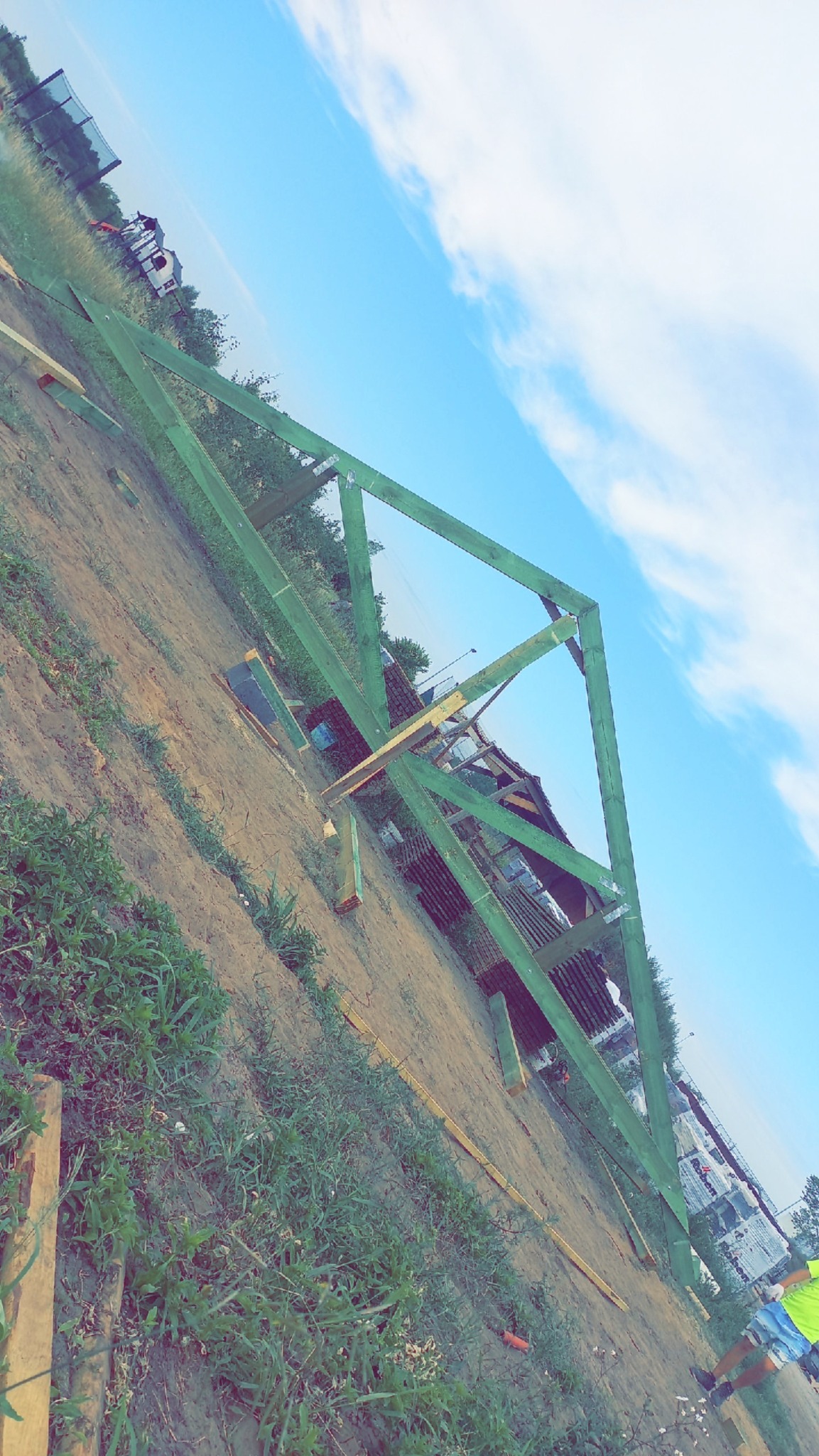 Wznoszenie zielonej więźby dachowej na placu budowy. Widoczne elementy drewniane i niebo w tle. Kąt ujęcia z dołu podkreśla konstrukcję dachu.