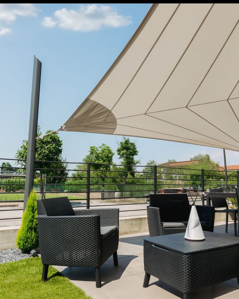 Nowoczesny taras z beżową, trójkątną osłoną przeciwsłoneczną, czarnymi meblami rattanowymi i zielonym trawnikiem, otoczony czarną balustradą.