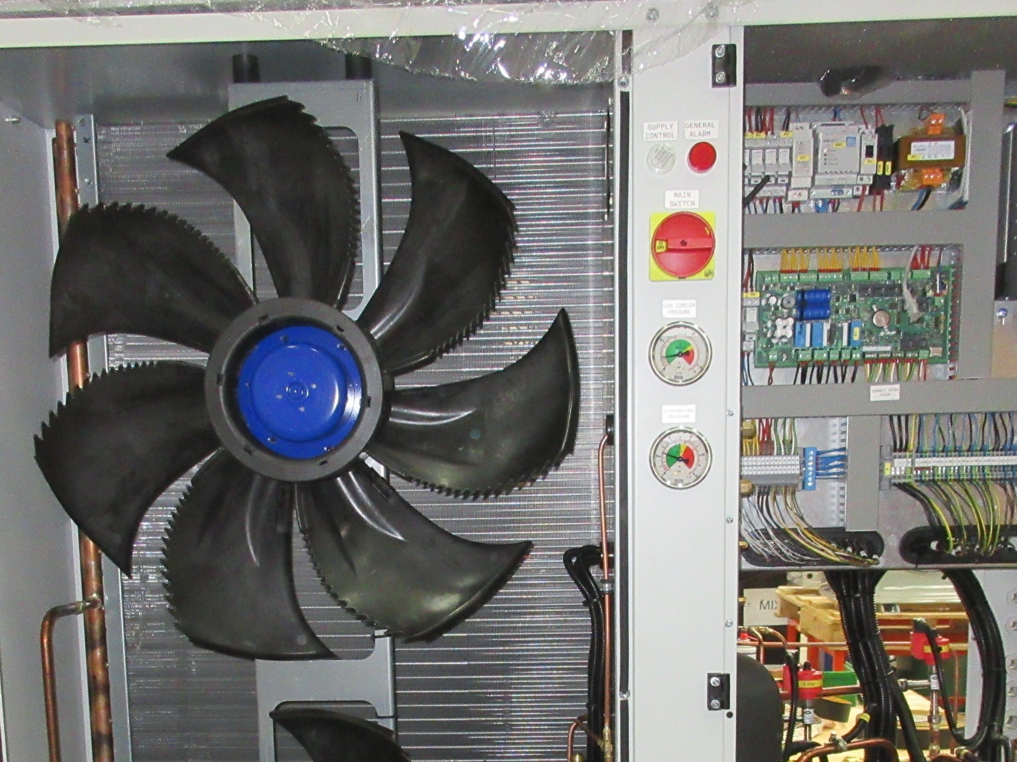 Wnętrze jednostki klimatyzacyjnej z wentylatorem, okablowaniem i panelem sterowania. Widoczne manometry i przełączniki. Detal techniczny urządzenia chłodniczego.