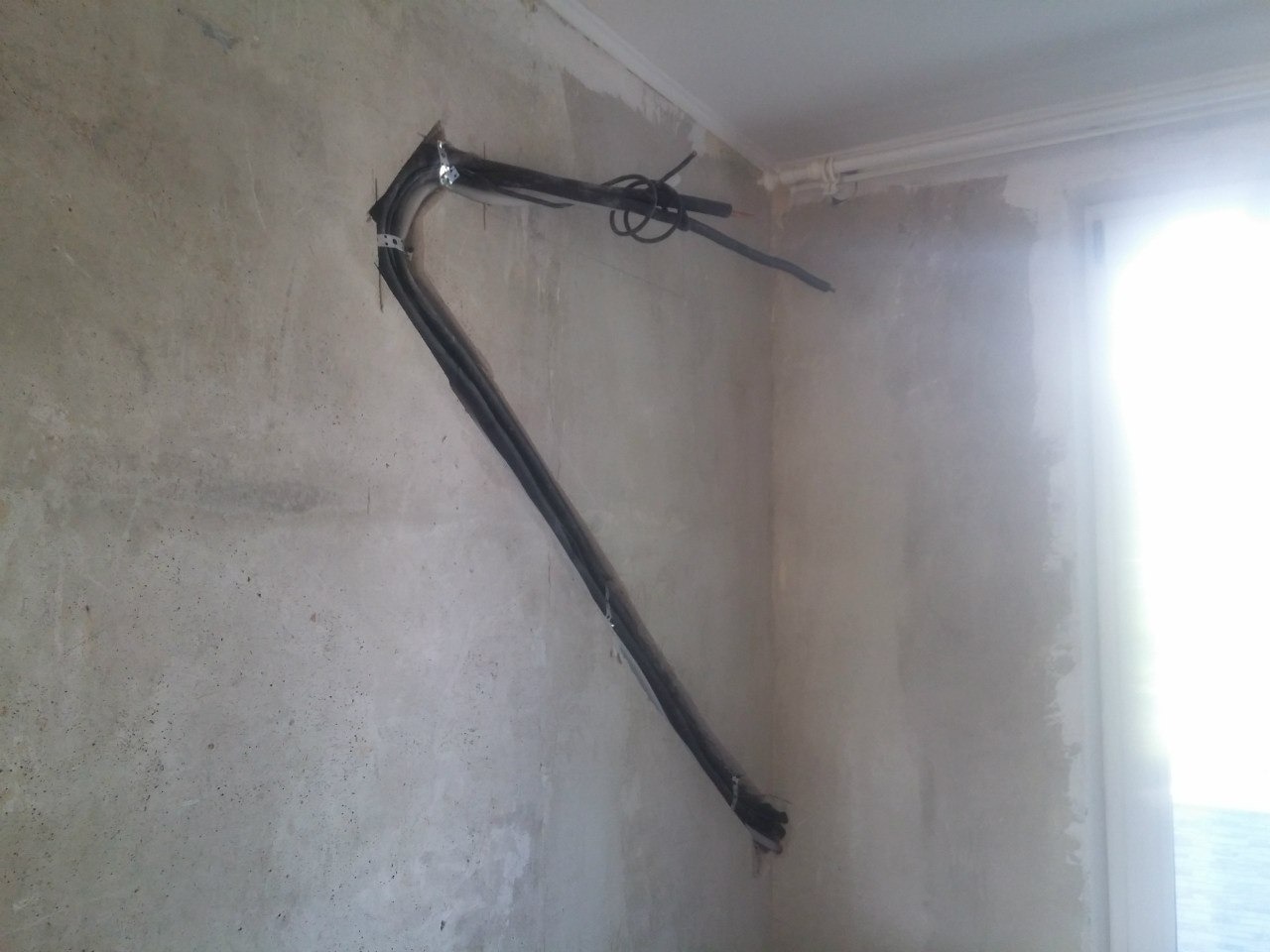 Montaż przewodów klimatyzacji na surowej ścianie z widocznymi mocowaniami. Kable prowadzone wzdłuż ściany, przygotowane do dalszej instalacji systemu.