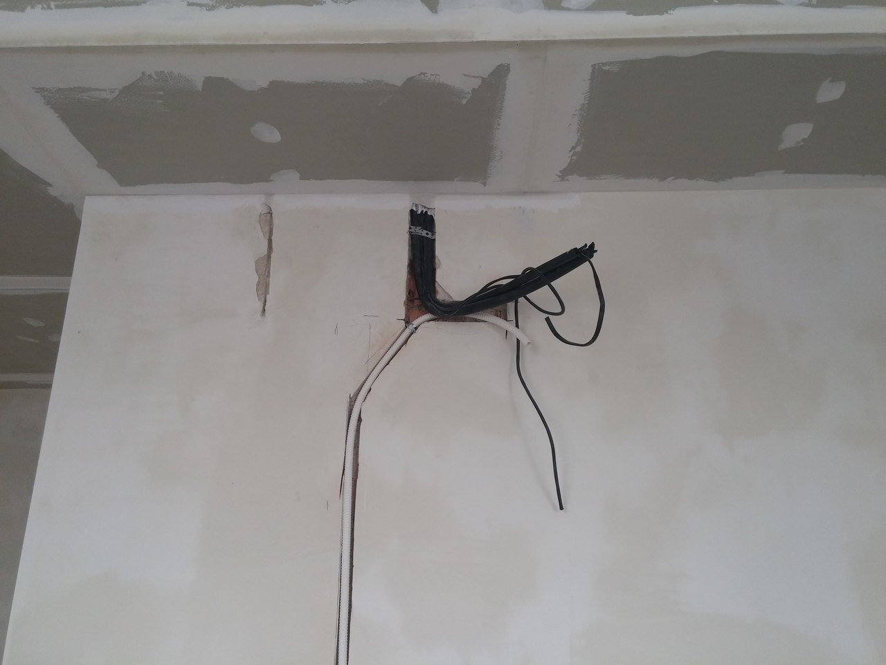 Montaż instalacji klimatyzacji w ścianie: widoczne przewody elektryczne i rurki chłodnicze w bruzdach, sufit z płyt gipsowo-kartonowych w trakcie wykończenia.