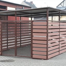 SHIPSTEEL MATEUSZ SKOPIŃSKI - Zadaszona wiata śmietnikowa z brązowymi, poziomymi panelami i metalową siatką, stojąca na szarym bruku. W tle budynki mieszkalne i gospodarcze.