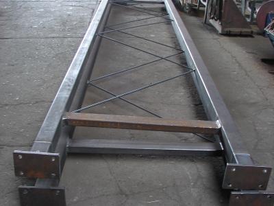 Metalowa konstrukcja schodów z poprzecznymi wzmocnieniami, widoczne spawy. Surowy stan, przygotowana do montażu. Szara kolorystyka, industrialny charakter.