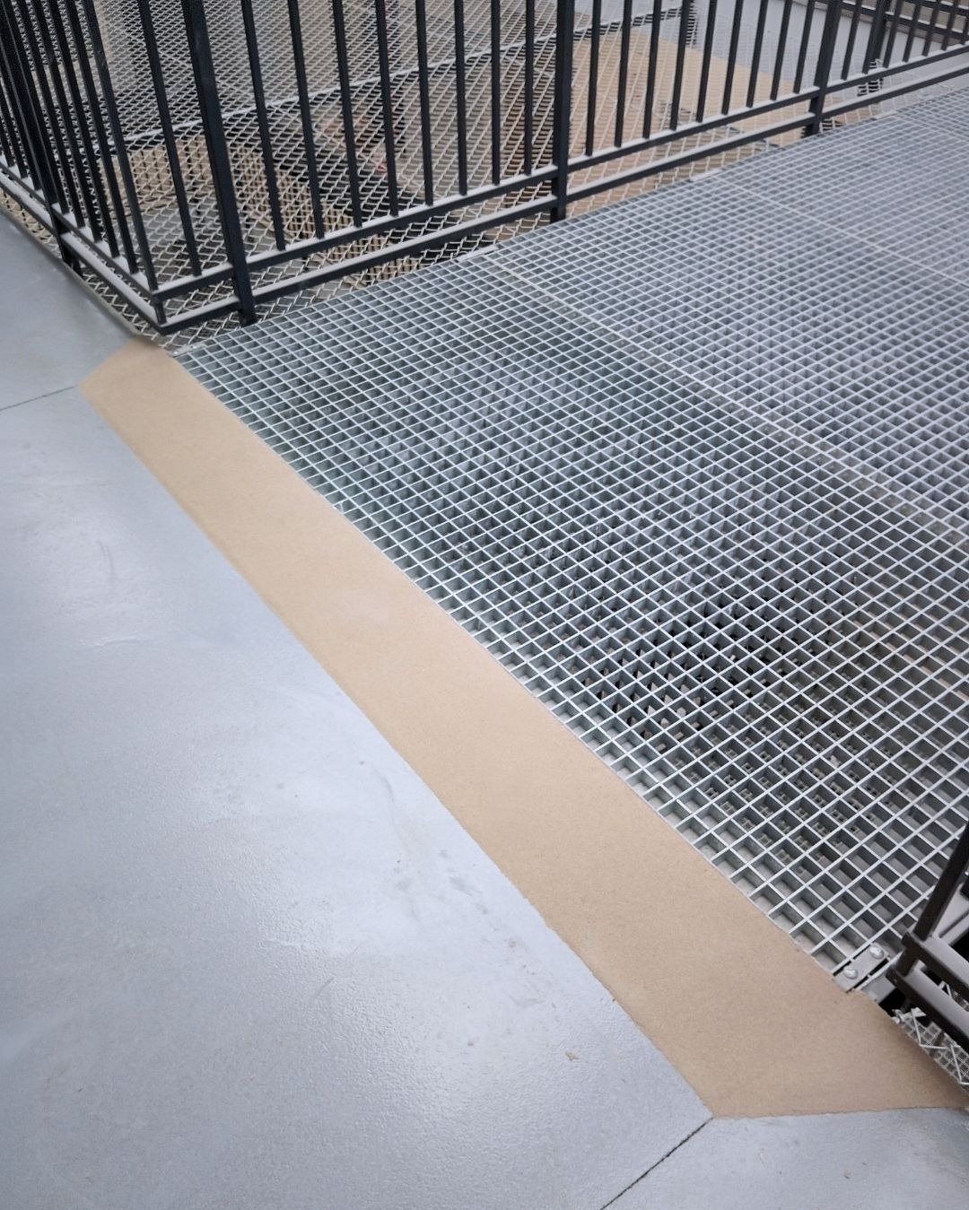 Metalowa krata pomostowa z obrzeżem na szarej posadzce w Nysie. Widoczne elementy konstrukcji i barierki. Detal wykończenia podłogi.