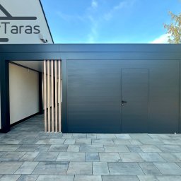 IwTaras - Nowoczesna, grafitowa zabudowa tarasu z drewnianymi lamelami, widoczna z zewnątrz na tle kostki brukowej i fragmentu budynku z logo firmy.