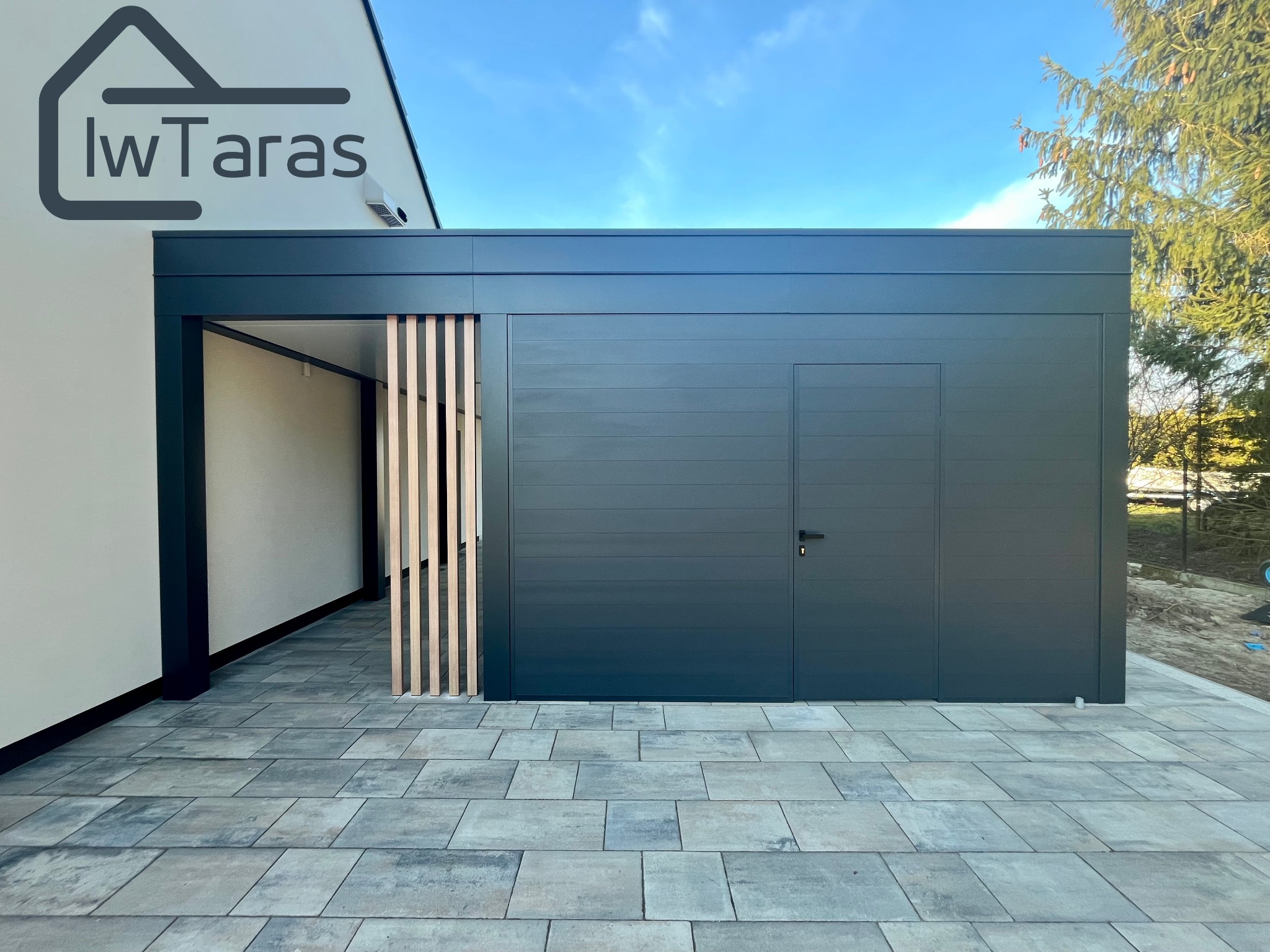 Nowoczesna, grafitowa zabudowa tarasu z drewnianymi lamelami, widoczna z zewnątrz na tle kostki brukowej i fragmentu budynku z logo firmy.