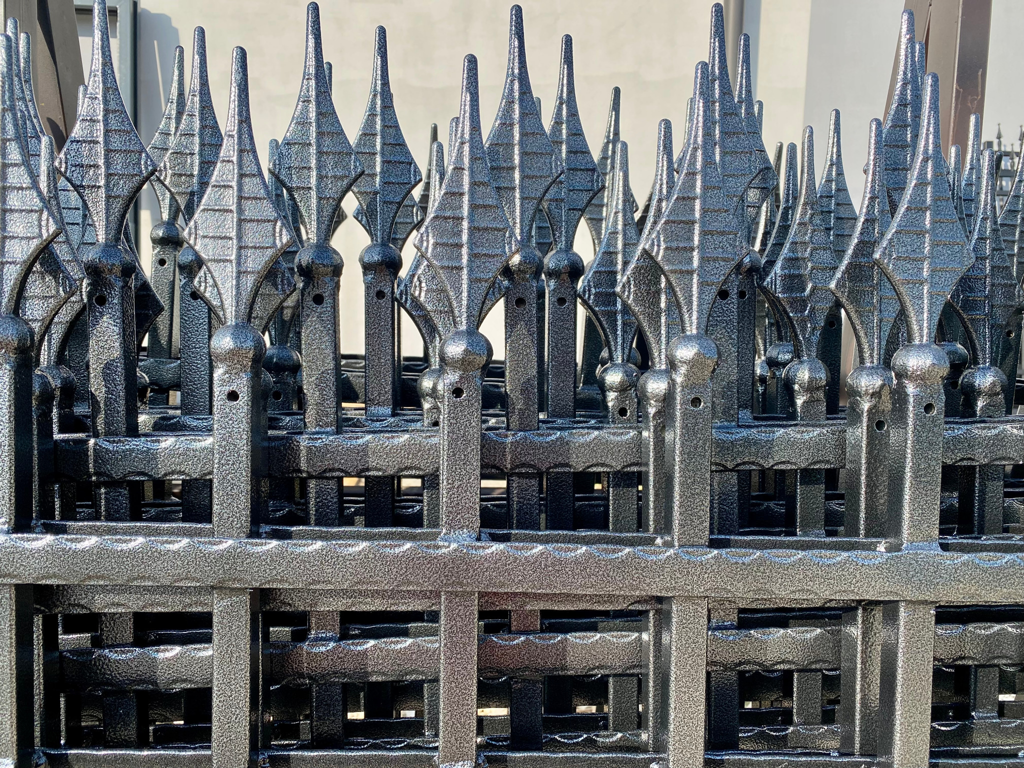 Szereg metalowych przęseł ogrodzeniowych w kolorze stal antyczna, z dekoracyjnymi grotami i kulistymi elementami, ustawionych jeden za drugim.