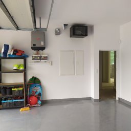 Eletrik - Wykończony garaż z szarą, błyszczącą posadzką żywiczną, regałem, instalacją elektryczną z inwerterem Fronius i szafką RACK na ścianie.