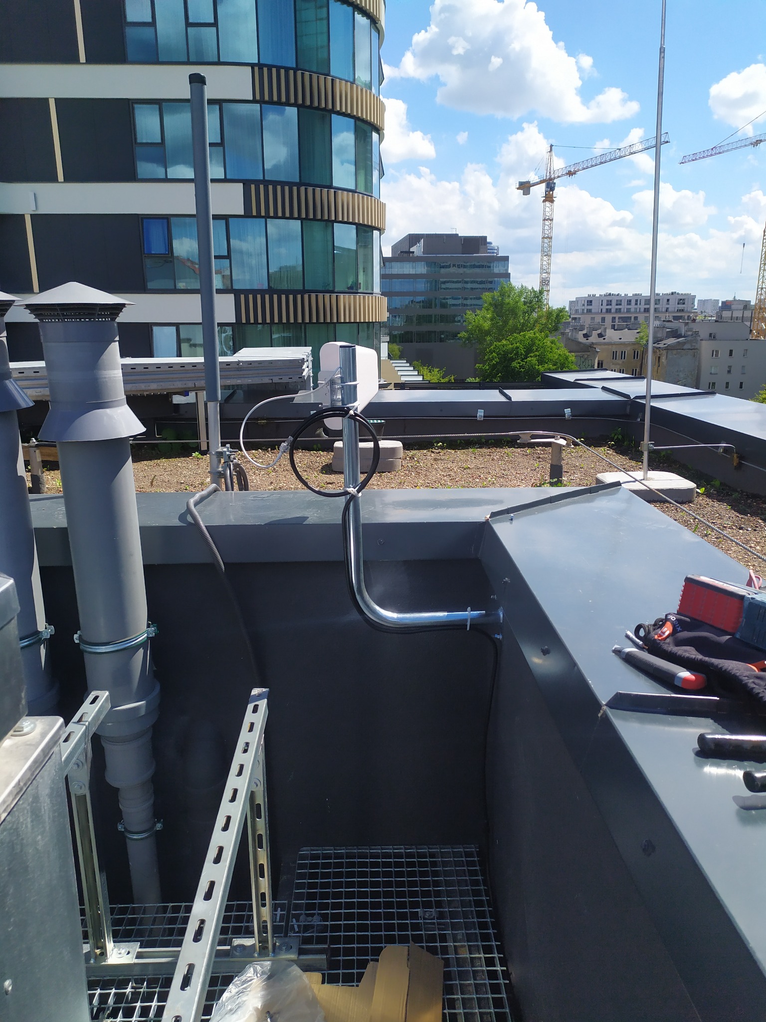 Instalacja odgromowa na dachu budynku: przewody, uziemienie, uchwyty. W tle miejski krajobraz z dźwigami budowlanymi i nowoczesną architekturą.