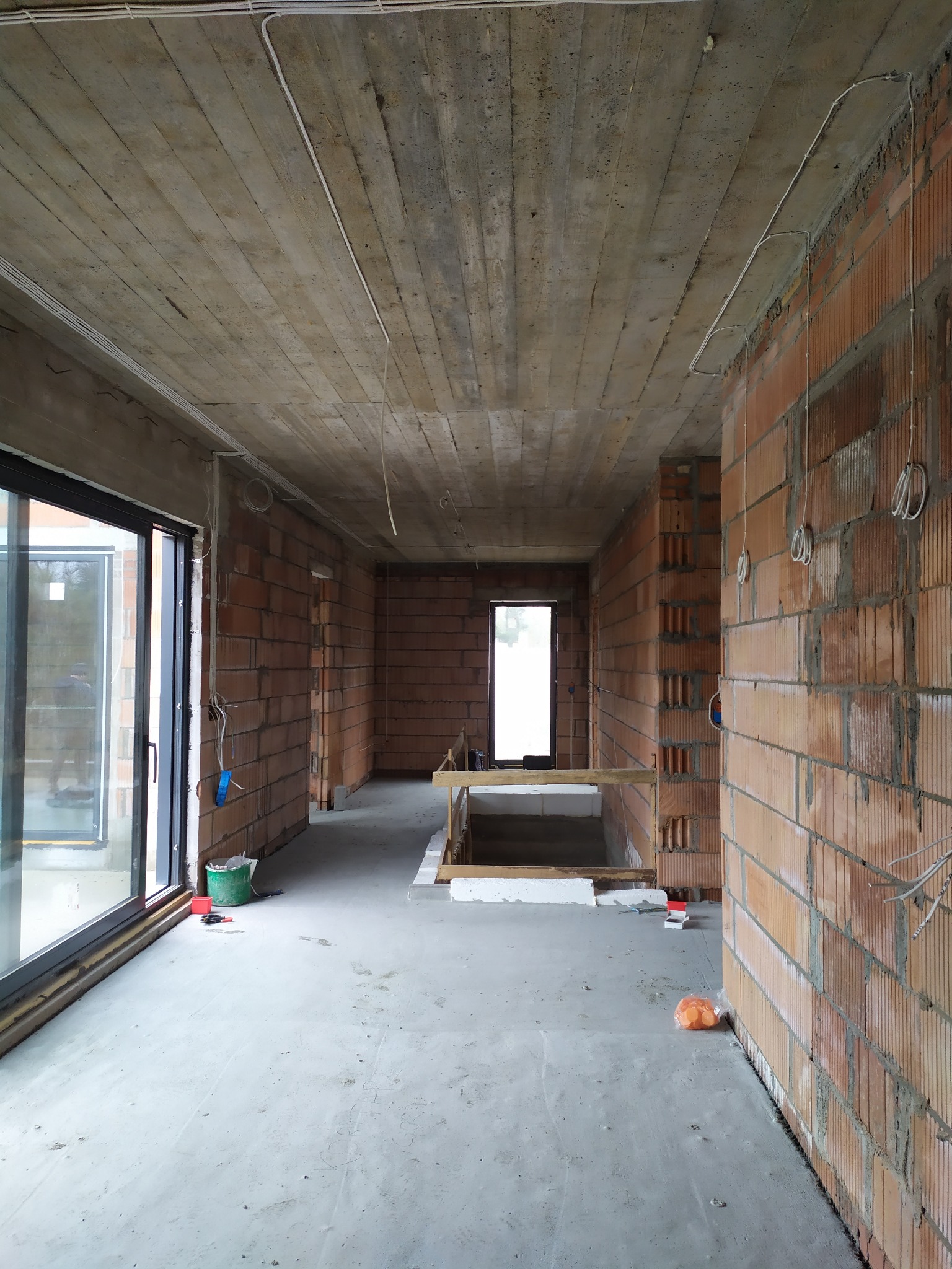 Surowy stan wnętrza budynku z widoczną instalacją elektryczną na suficie i ścianach z cegły. Widoczne kable i puszki elektryczne przed tynkowaniem.