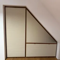 Beżowe plisy okienne w drewnianej ramie, dopasowane do skosu poddasza. Widok na drewnianą podłogę.