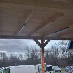 MR-Elektro - Drewniana konstrukcja z zamontowanym oświetleniem LED, widoczna drabina i samochody w tle. Oświetlenie pod zadaszeniem.