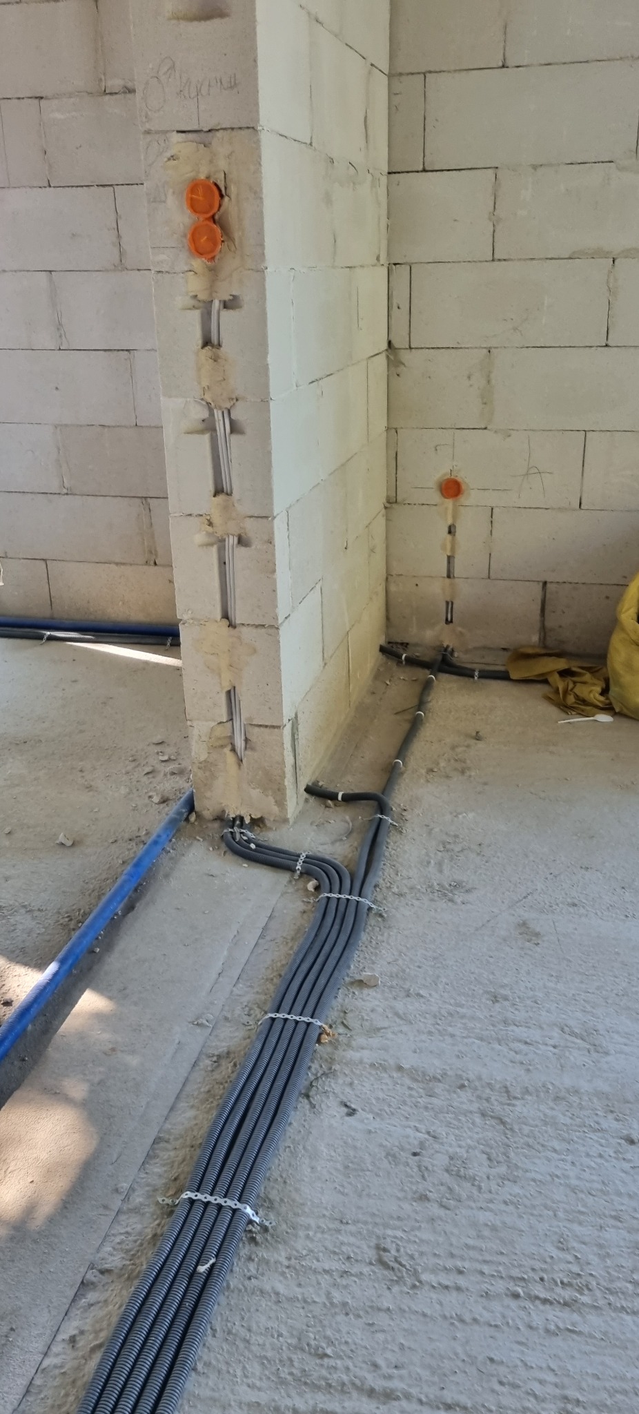 Instalacja elektryczna w surowym budynku: kable w peszlach przymocowane do ściany z betonu komórkowego, widoczne puszki instalacyjne. Etap prac przed tynkowaniem.