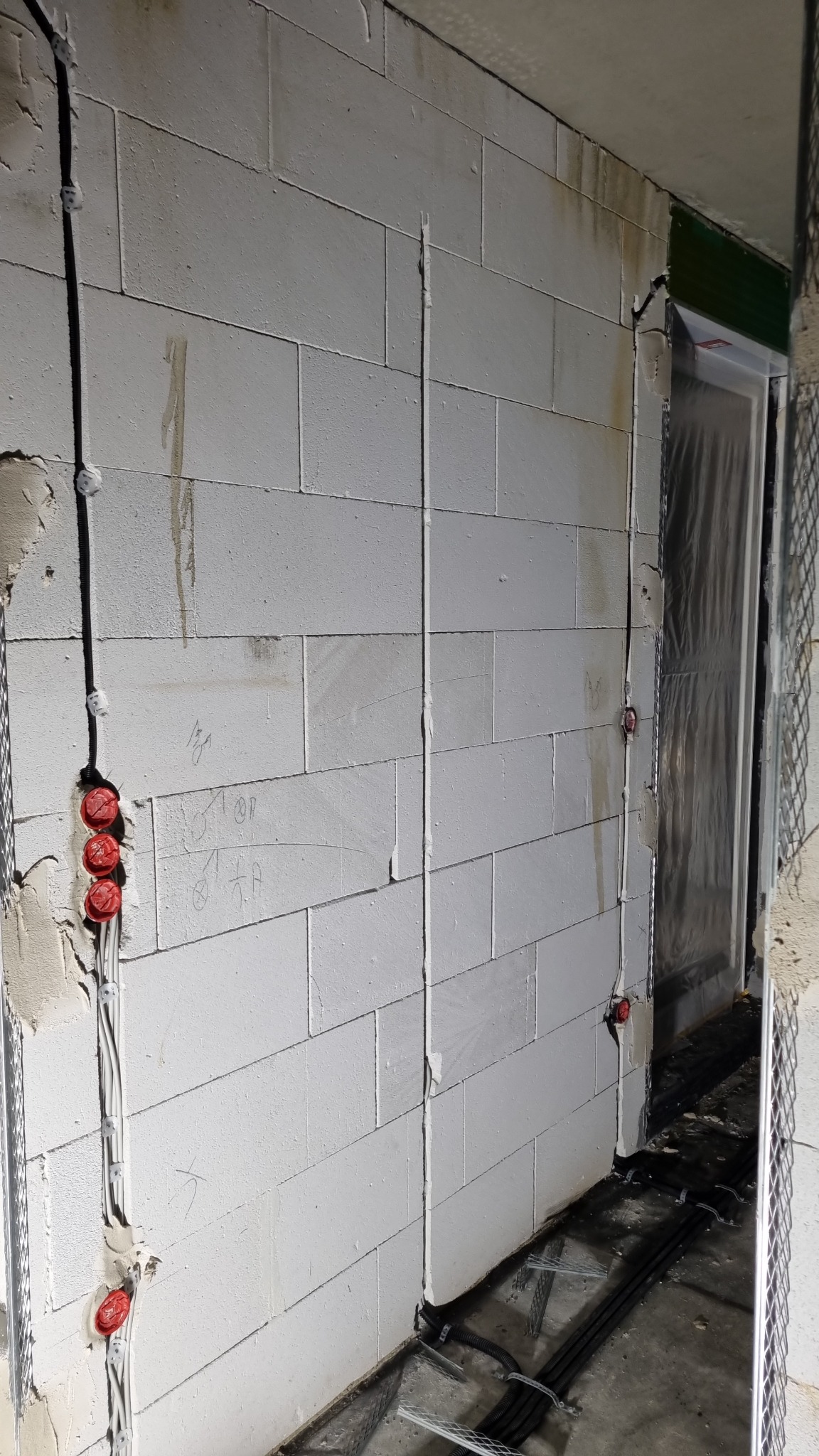 Wewnętrzna instalacja elektryczna w trakcie montażu, kable prowadzone po ścianie z betonu komórkowego, widoczne puszki instalacyjne i przewody. Etap prac w nowym budownictwie.