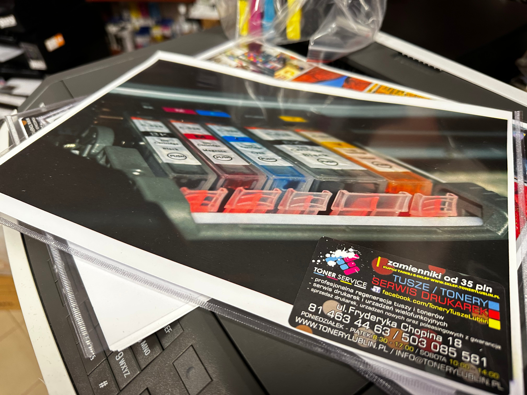 Zdjęcie kartridży do drukarki, z naklejką firmy serwisującej tonery i drukarki, leżące na kserokopiarce. Widoczny fragment klawiatury kserokopiarki.